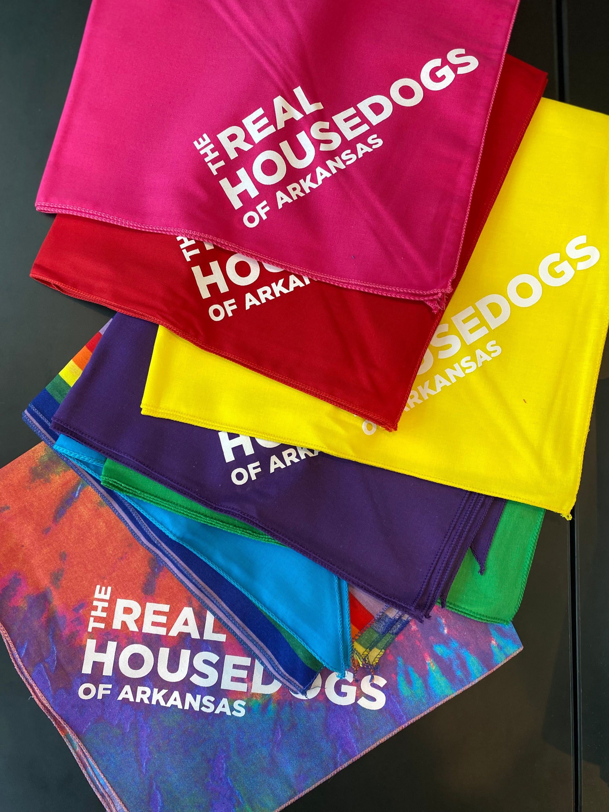 Stack of colorful bandanas with 'The Real Housedogs of Arkansas' text on a dark surface.