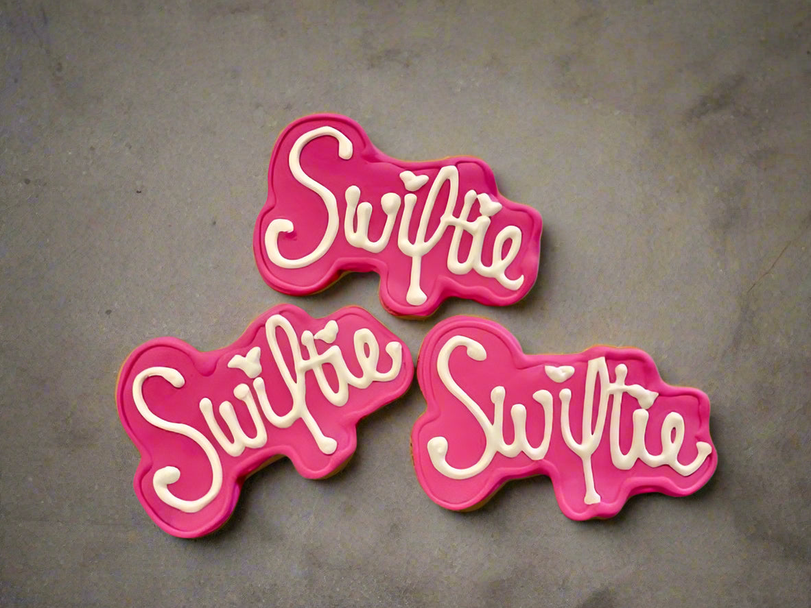 Three pink and white 'Swiftie' dog cookies on a gray background
