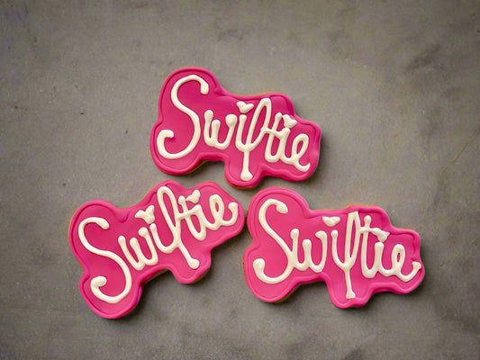Three pink and white 'Swiftie' dog cookies on a gray background