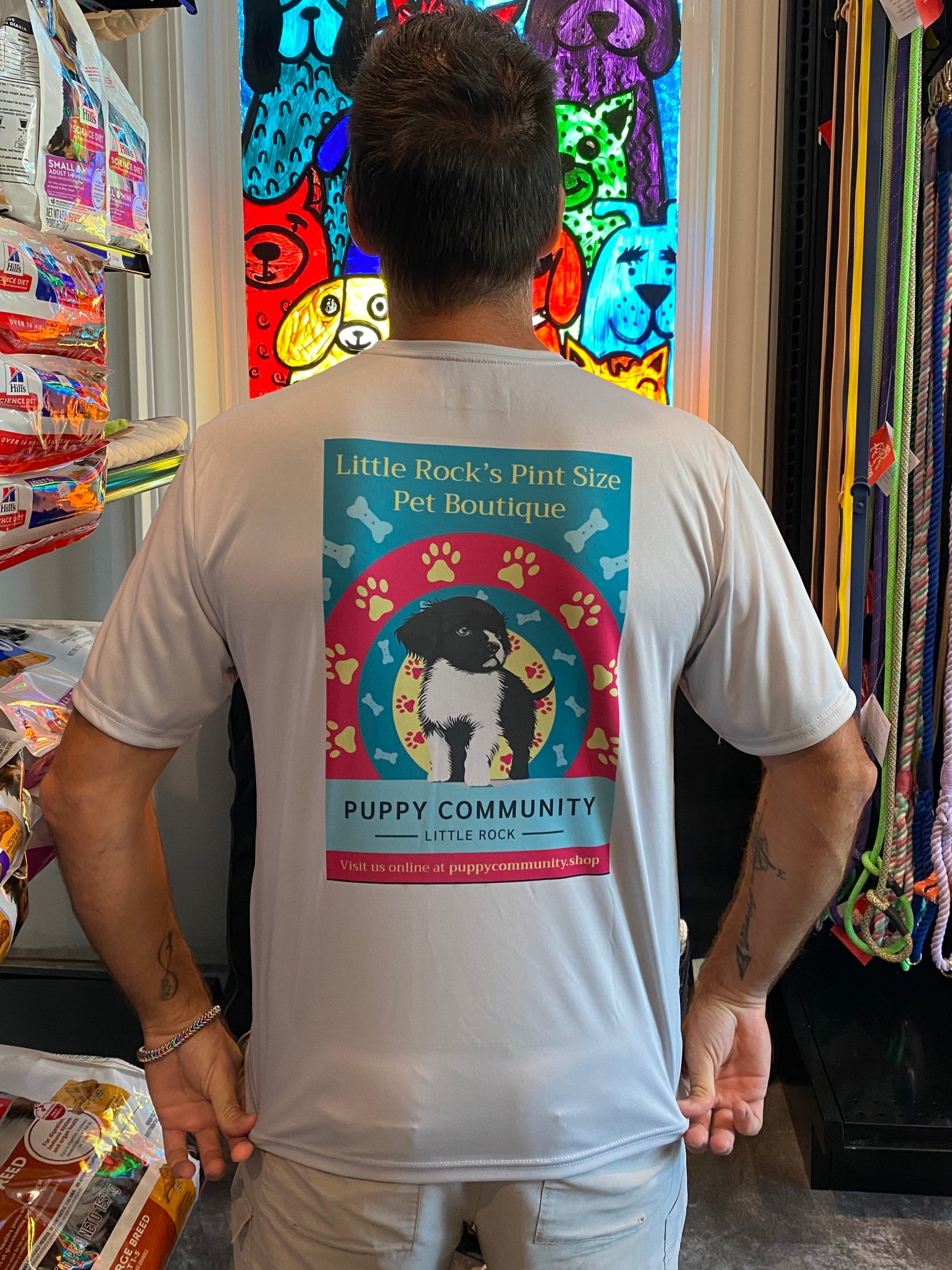 Person wearing a t-shirt with a colorful graphic design in front of a window display.